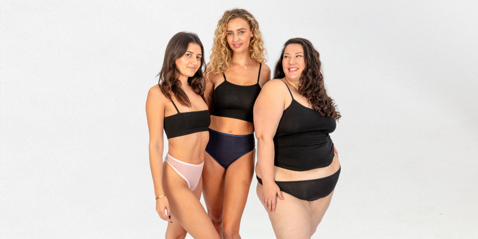 image of three women in ugly pants period pants. The woman on the left is wearing the blush high waisted period thong, the woman in the middle is wearing the navy high waisted period pants and the woman on the right is wearing black period pants
