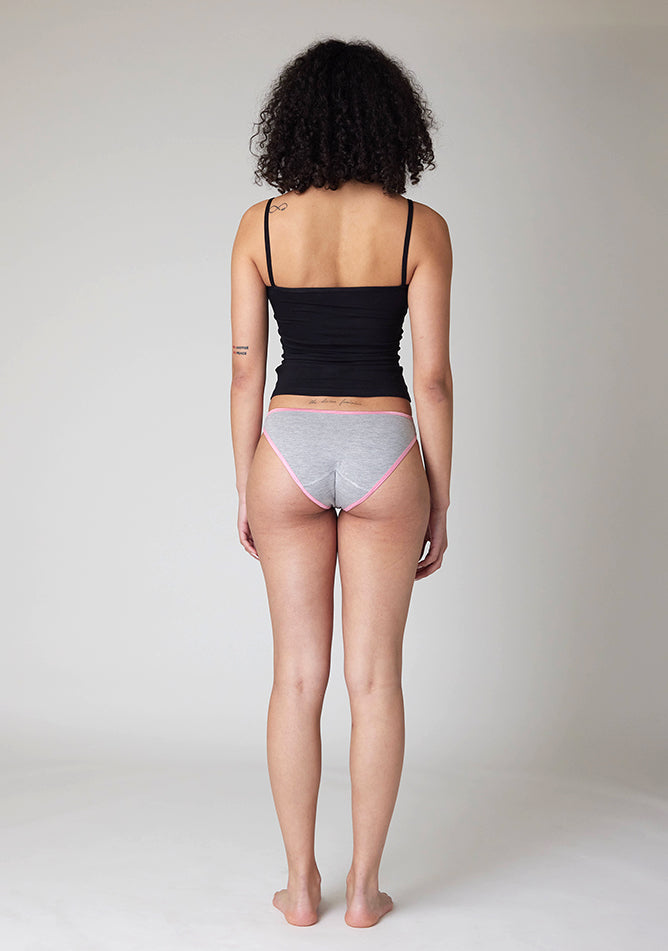 Back image of a five-foot-ten, size 10 model wearing Ugly Pants' Grey Bikini Brief period Pants with light pink elastic in moderate to heavy absorbency, paired with a black cami top