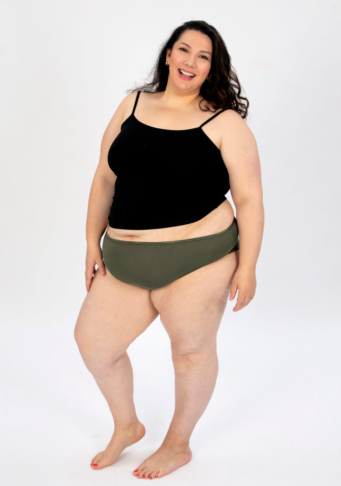 Front quarter image of a five foot seven, size 22 model wearing Ugly Pants' olive high waisted period pants in light to moderate absorbency, paired with a black crop top.