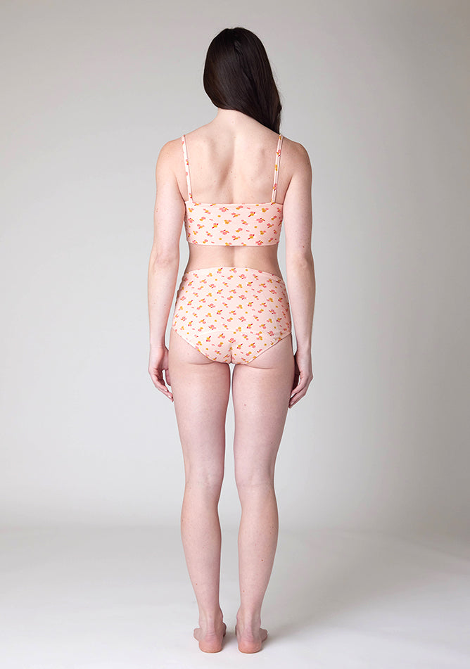 Back image of a five-foot-nine, size 8 model wearing Ugly Pants' Pink Floral Print Overnight period pants in moderate to heavy absorbency, paired with a pink floral print crop top, with a self tie detachable bow, this image does not feature the self tie bow, but a straight neckline.