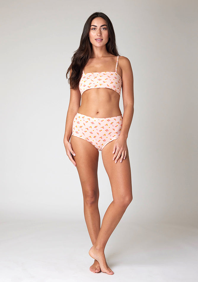 Front image of a five-foot-ten, size 10 model wearing Ugly Pants' Pink Floral Print Overnight period pants in moderate to heavy absorbency, paired with a pink floral print crop top, with a self tie detachable bow, this image does not feature the self tie bow, but a straight neckline.