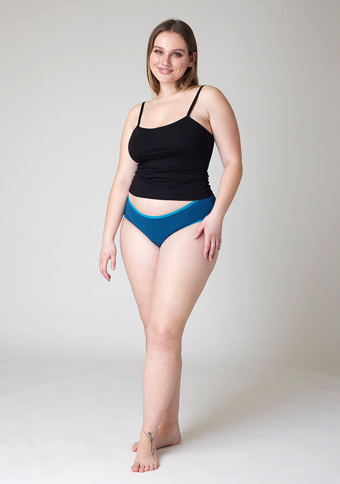 Front image of a five-foot-five, size 14 model wearing Ugly Pants' Teal Hipster Brief Period Pants in light to moderate absorbency, paired with a black cami top