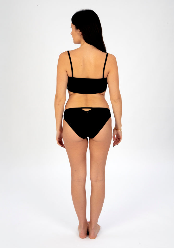 Back image of a five foot six, size 8 model wearing Ugly Pants' Black Lace Bikini Brief Period Pant in a light to moderate absorbency, paired with a black crop top.