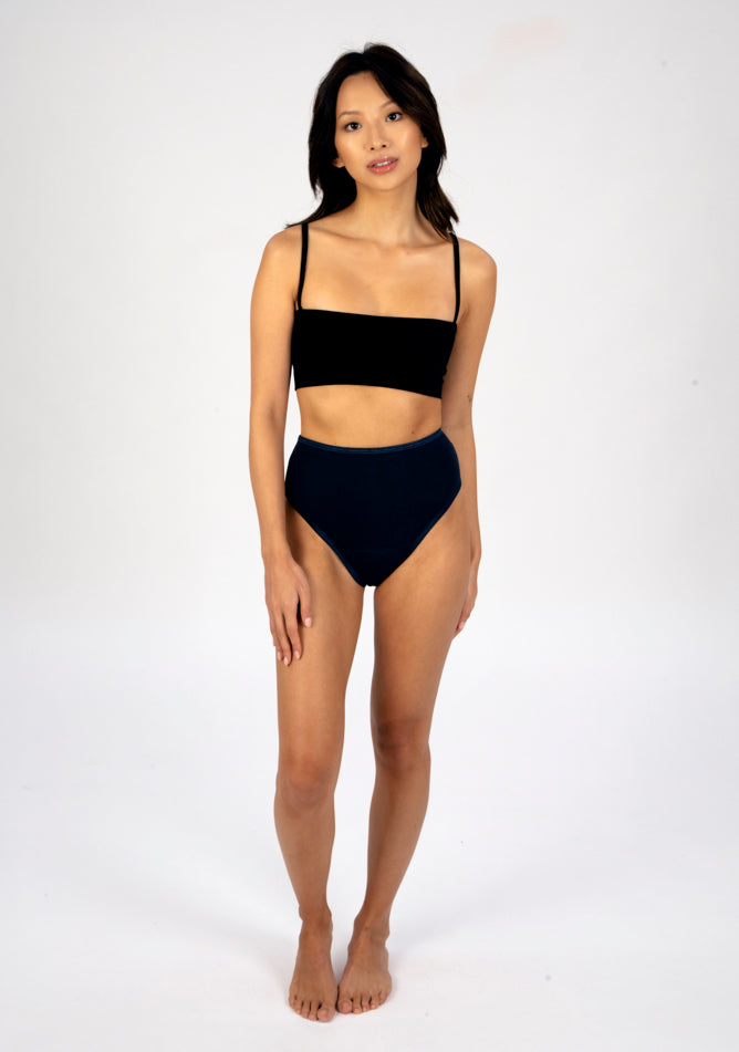 Front image of a five foot three, size 6 model wearing Ugly Pants' navy high waisted period pants in light to moderate absorbency, paired with a black crop top.