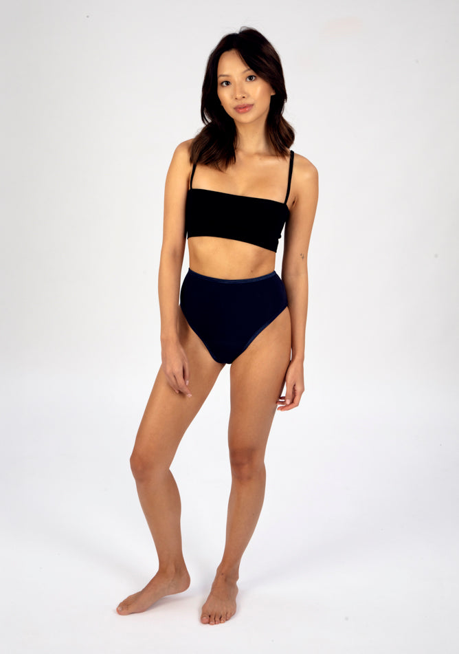 Front quarter image of a five foot three, size 6 model wearing Ugly Pants' navy high waisted period pants in light to moderate absorbency, paired with a black crop top.