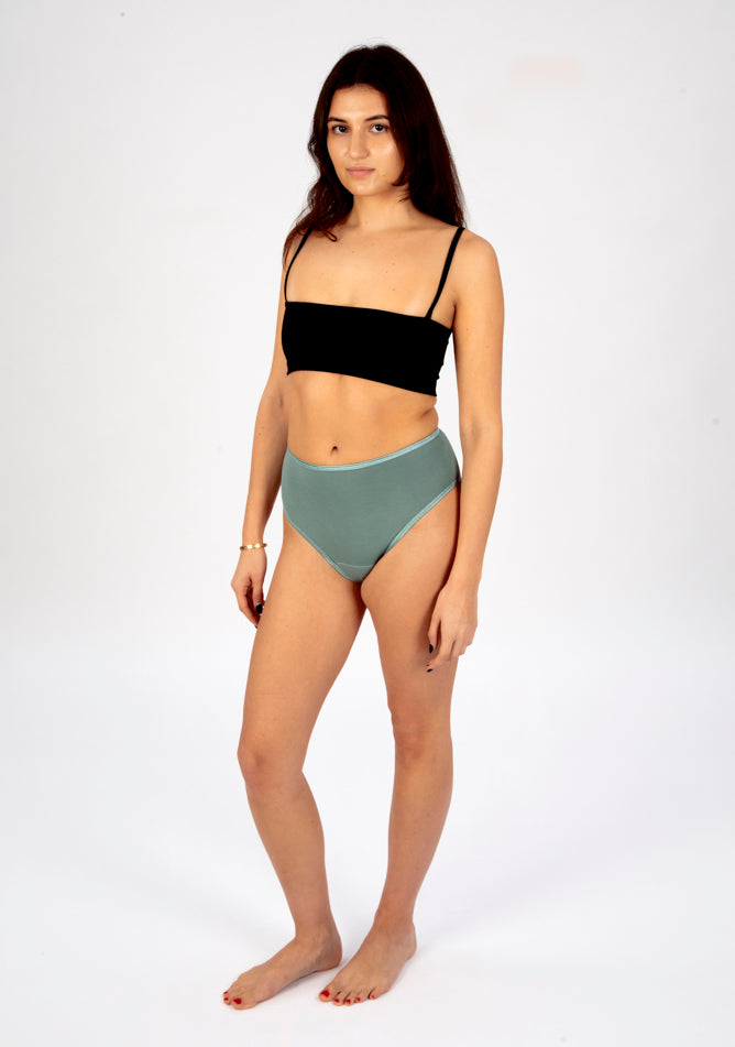 Front quarter image of a five foot six, size 8 model wearing Ugly Pants' sage high waisted period pants in moderate to heavy absorbency, paired with a black cami top.