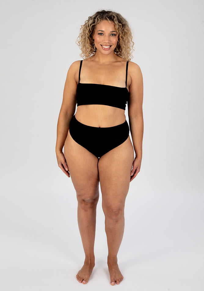 Front image of a five foot seven, size 16 model wearing Ugly Pants' black high waisted period pants in light to moderate absorbency, paired with a black crop top.