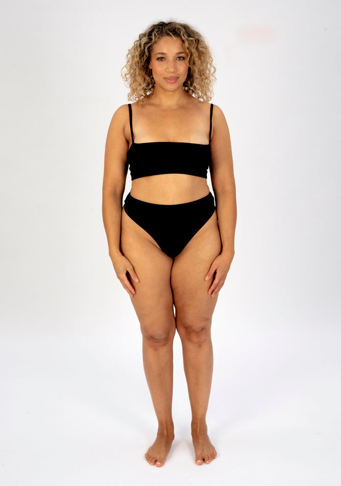 Front image of a five foot seven, size 16 model wearing Ugly Pants' black high waisted period thong in light absorbency, paired with a black crop top.