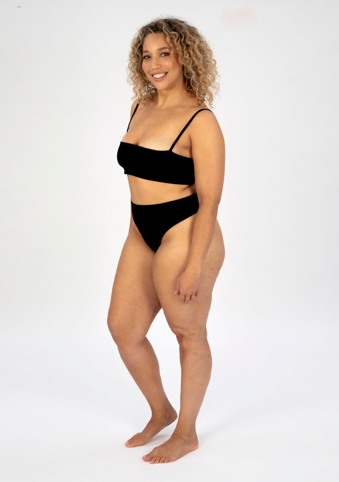 Front quarter image of a five foot seven, size 16 model wearing Ugly Pants' black high waisted period thong in light absorbency, paired with a black crop top.