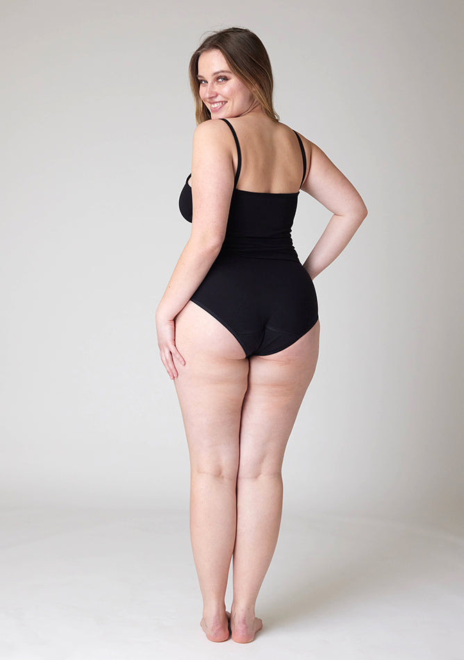 Back image of a five-foot-five, size 14 model wearing Ugly Pants' Black Hipster Brief Period Pants in light to moderate  absorbency, paired with a black cami top