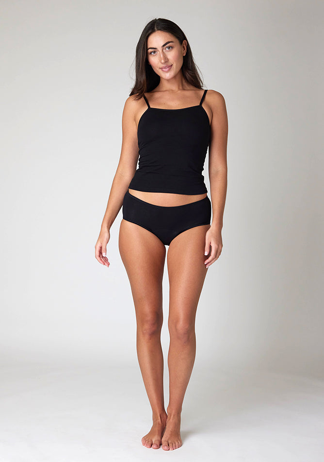 Front image of a five-foot-ten, size 10 model wearing Ugly Pants' Black Hipster Brief Period Pants in light to moderate  absorbency, paired with a black cami top