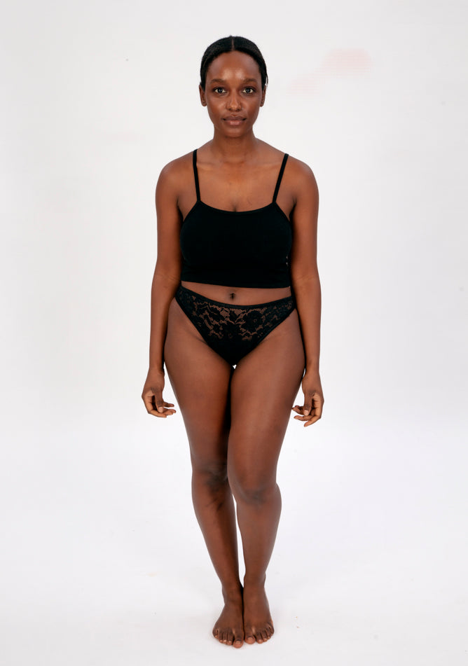 Front image of a five foot four, size 10 model wearing Ugly Pants' Black Lace Bikini Brief Period Pant in a light to moderate absorbency, paired with a black crop top.