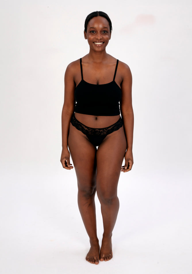 Front image of a five foot four, size 1o model wearing Ugly Pants' Black Lace Thong period pants in a light absorbency, paired with a black crop top.