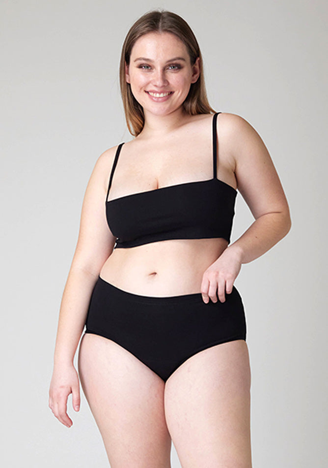 Close  up image of a five-foot-five, size 14 model wearing Ugly Pants' black Overnight period pants in moderate to heavy absorbency, paired with a black crop top, this image does not feature the self tie bow, but a straight neckline. 