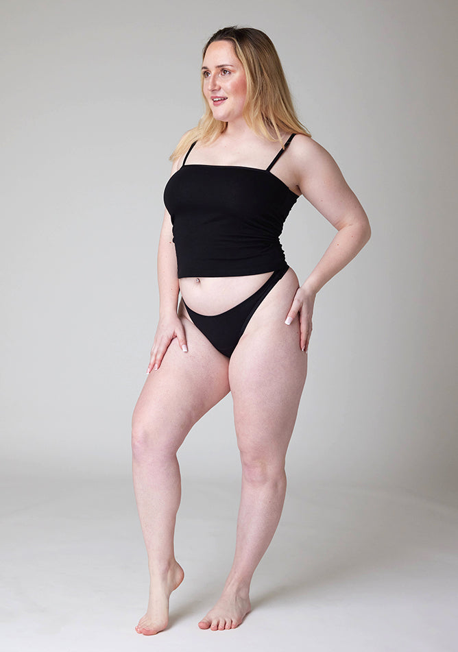 Front quarter image of a five-foot-three, size 12 model wearing Ugly Pants' Black Thong period pants in a light absorbency, paired with a black cami top.