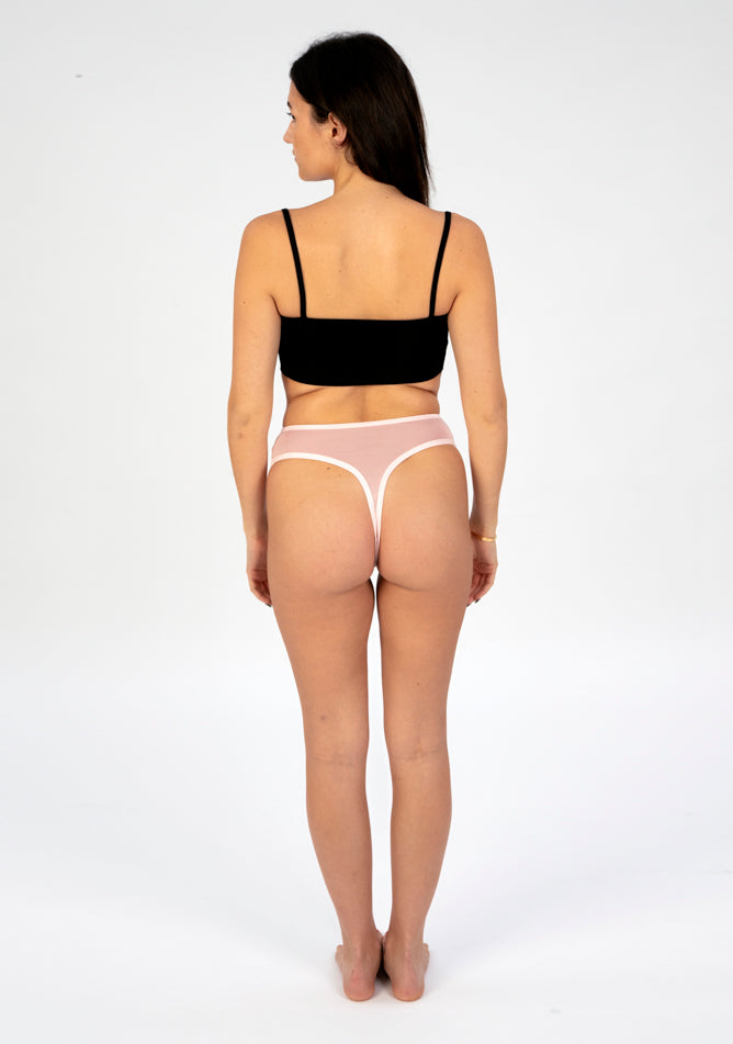 Back image of a five foot six, size 8 model wearing Ugly Pants' blush high waisted period thong in light absorbency, paired with a black crop top.