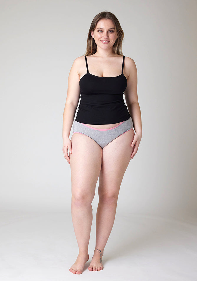Front image of a five-foot-five, size 14 model wearing Ugly Pants' Grey Hipster Brief Period Pants with light pink elastic in light to moderate  absorbency, paired with a black cami top