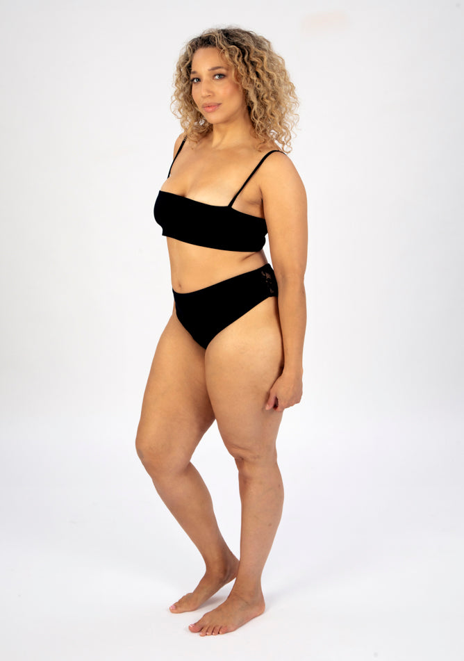 Front quarter image of a five foot sveen, size 16 model wearing Ugly Pants' Black Lace High Waisted Period Pant in a light to moderate absorbency, paired with a black crop top.