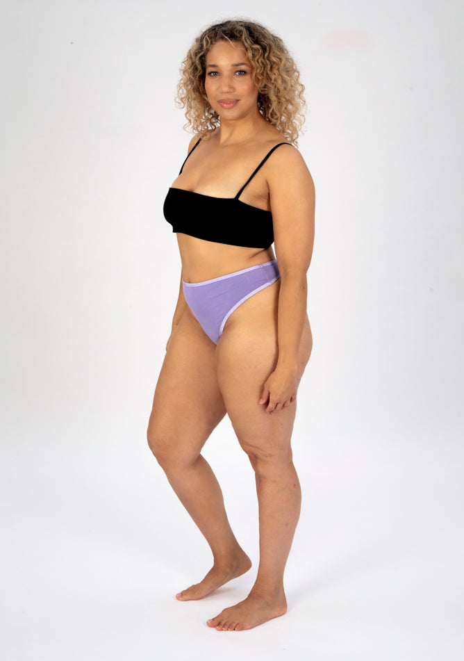 Front quarter image of a five foot seven, size 16 model wearing Ugly Pants' lilac high waisted period thong in light absorbency, paired with a black crop top.