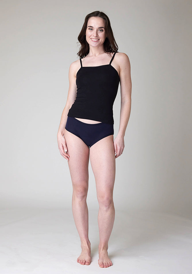 Front image of a five-foot-nine, size 8 model wearing Ugly Pants' Navy Hipster Brief Period Pants in moderate to heavy absorbency, paired with a black cami top