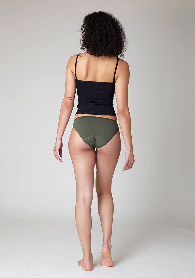 Back image of a five foot ten, size 10 model wearing Ugly Pants' Olive Bikini Brief period Pants in light to moderate absorbency, paired with a black cami top
