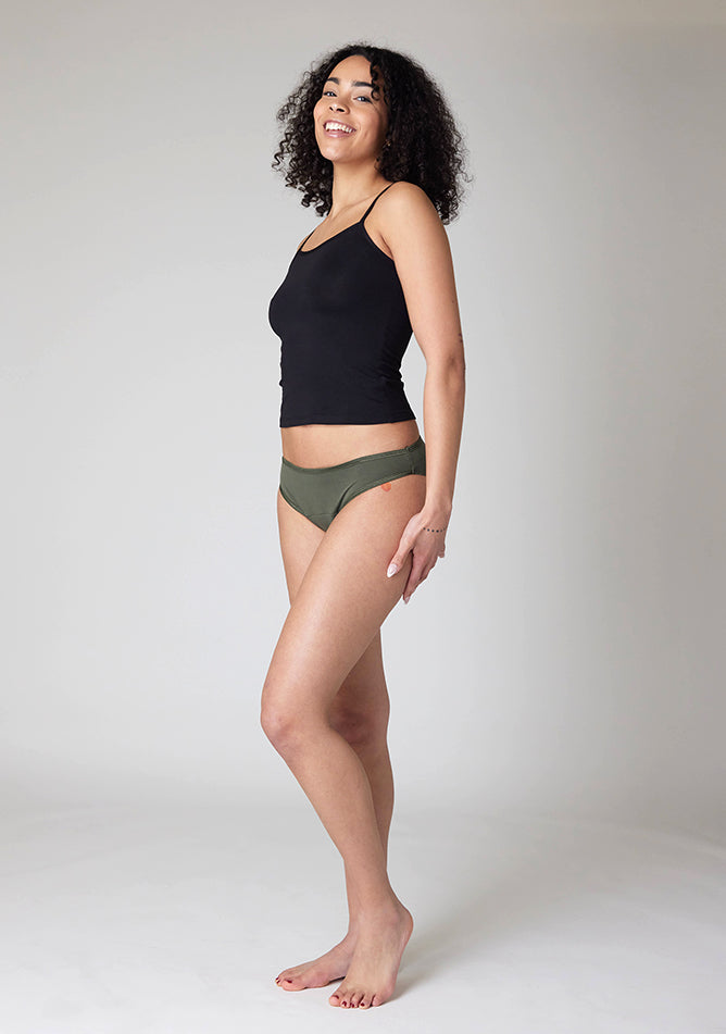Front quarter image of a five-foot-ten, size 10 model wearing Ugly Pants' Olive Bikini Brief period Pants in light to moderate absorbency, paired with a black cami top