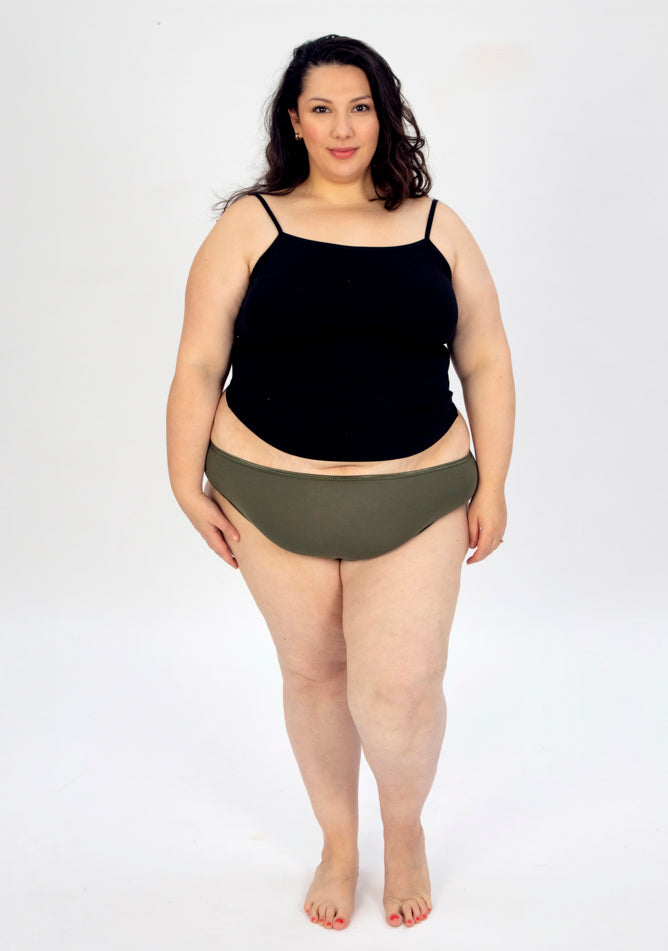 Front image of a five foot seven, size 22 model wearing Ugly Pants' olive high waisted period pants in light to moderate absorbency, paired with a black crop top.