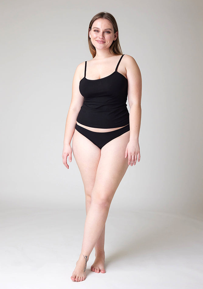 Front image of a five foot five, size 14 model wearing Ugly Pants' Black Bikini Brief period pants in light to moderate absorbency, paired with a black cami top.