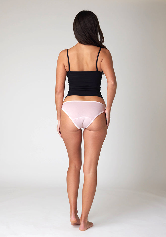 Back image of a five foot ten, size 10 model wearing Ugly Pants' Blush Bikini Brief period Pants in moderate  to heavy absorbency, paired with a black cami top
