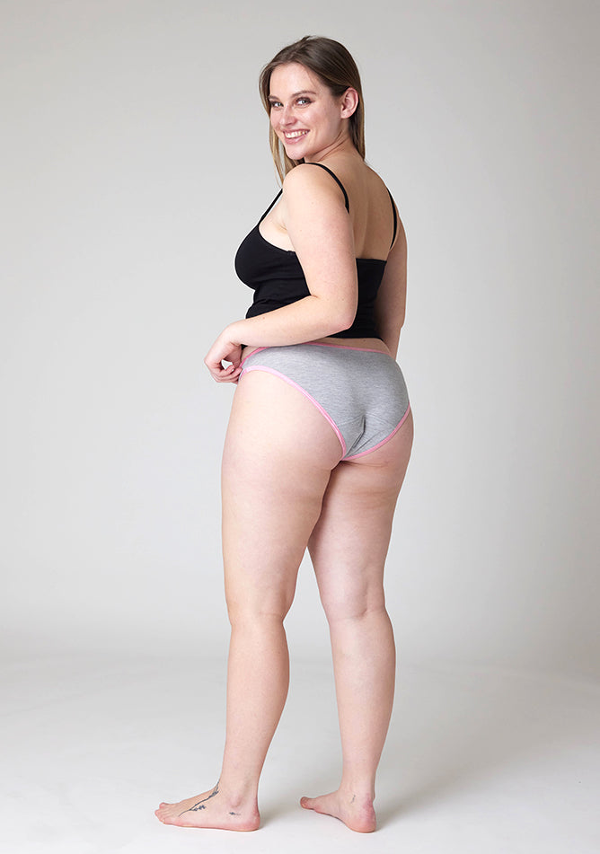 Quarter back image of a five foot five, size 14 model wearing Ugly Pants' Grey Bikini Brief period Pants with light pink elastic in moderate  to heavy absorbency, paired with a black cami top