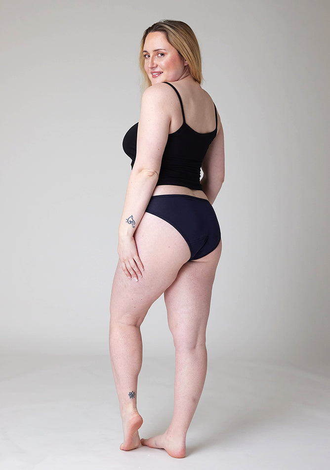 Quarter back image of a five foot three , size 12 model wearing Ugly Pants' Navy Bikini Brief period pants in light to moderate absorbency, paired with a black cami top. 