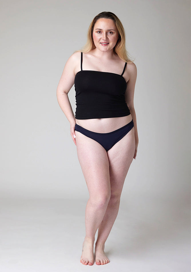 Front image of a five foot five , size 12 model wearing Ugly Pants' Navy Bikini Brief period pants in light to moderate absorbency, paired with a black cami top. 