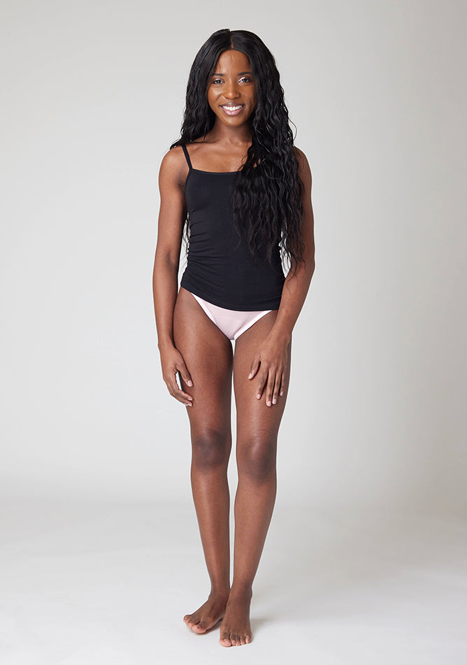 Front image of a five foot, size 6 model wearing Ugly Pants' Blush Bikini Brief period Pants in moderate  to heavy absorbency, paired with a black cami top