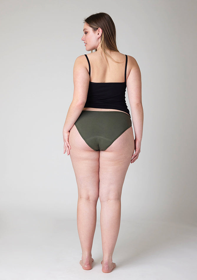 Back image of a five foot five, size 14 model wearing Ugly Pants' Olive Bikini Brief period Pants in light to moderate absorbency, paired with a black cami top