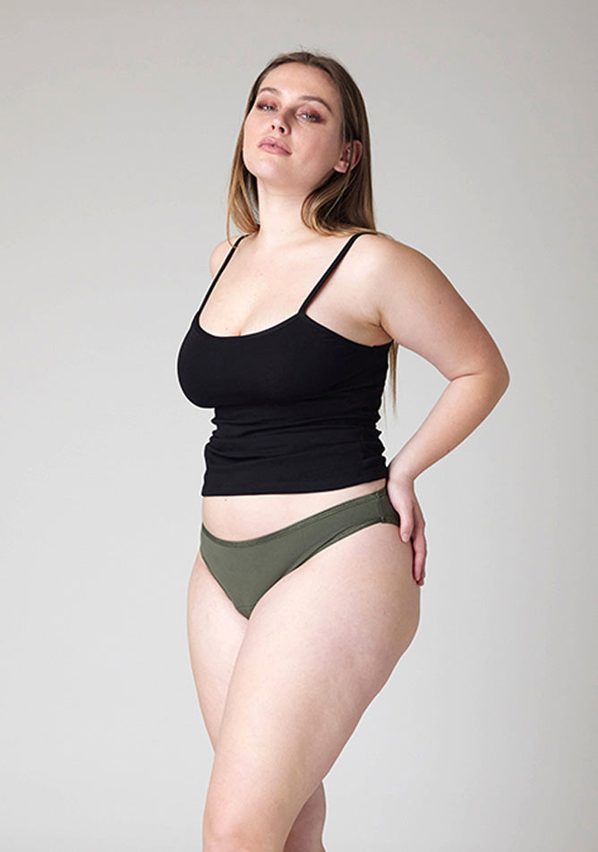 Close up quarter front image of a five foot five, size 14 model wearing Ugly Pants' Olive Bikini Brief period Pants in light to moderate absorbency, paired with a black cami top