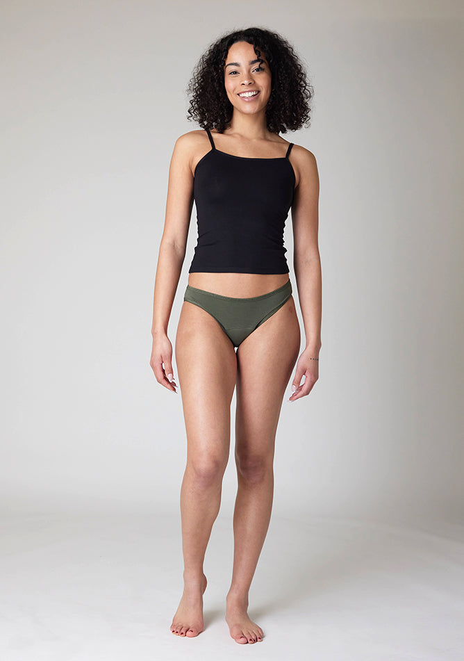 Front image of a five foot ten, size 10 model wearing Ugly Pants' Olive Bikini Brief period Pants in light to moderate absorbency, paired with a black cami top