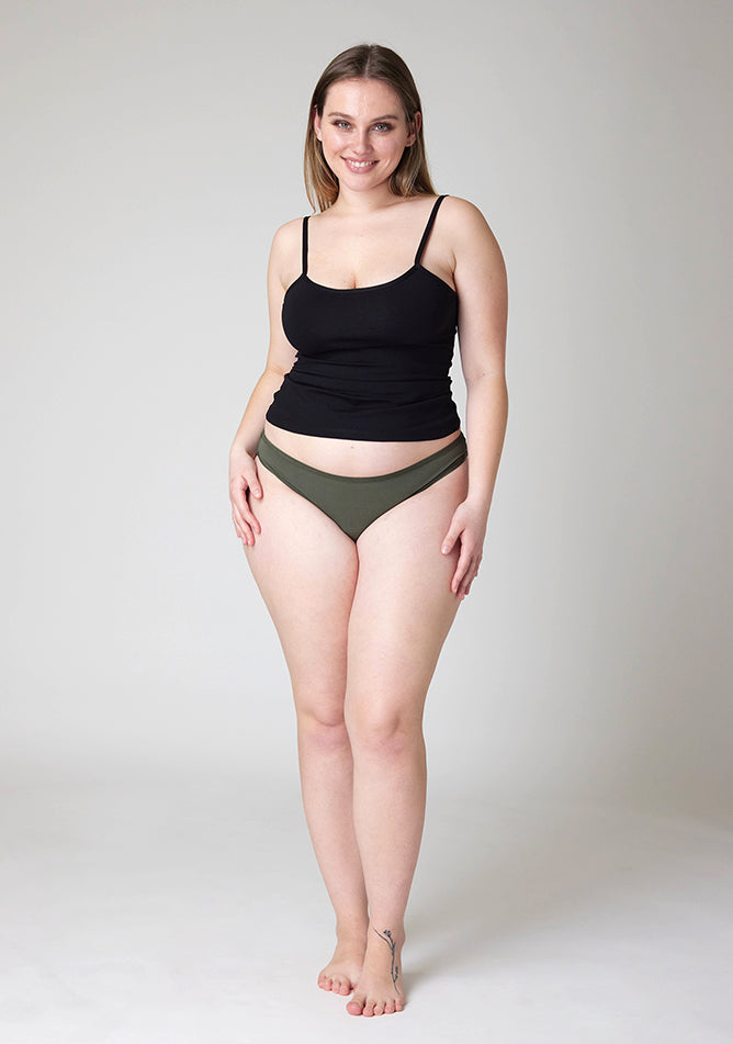 Front image of a five foot five, size 14 model wearing Ugly Pants' Olive Bikini Brief period Pants in light to moderate absorbency, paired with a black cami top