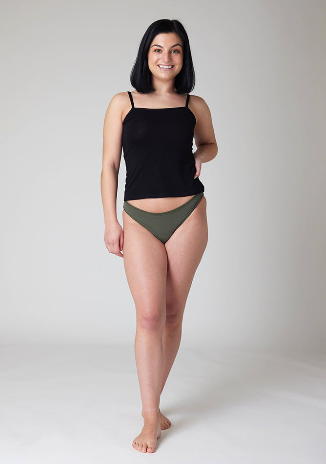 Front image of a five foot six, size 8 model wearing Ugly Pants' Olive Bikini Brief period Pants in moderate  to heavy absorbency, paired with a black cami top