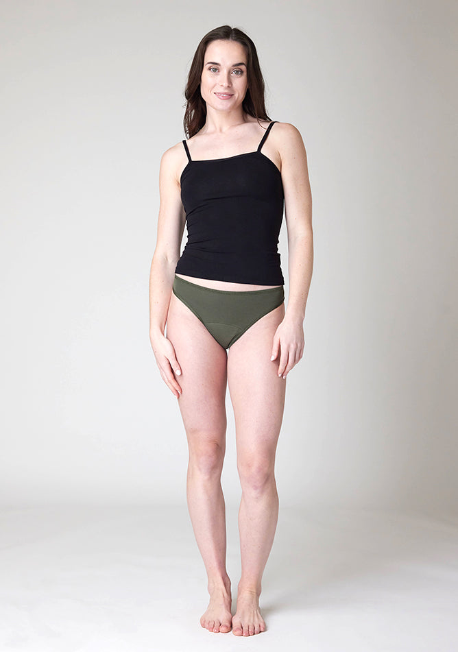 Front image of a five foot nine, size 8 model wearing Ugly Pants' Olive Bikini Brief period Pants in light to moderate absorbency, paired with a black cami top