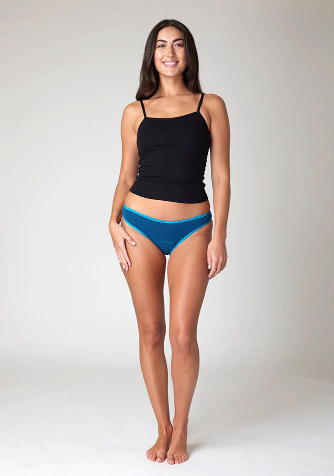 Front image of a five foot ten, size 10 model wearing Ugly Pants' Teal Bikini Brief period Pants in moderate  to heavy absorbency, paired with a black cami top