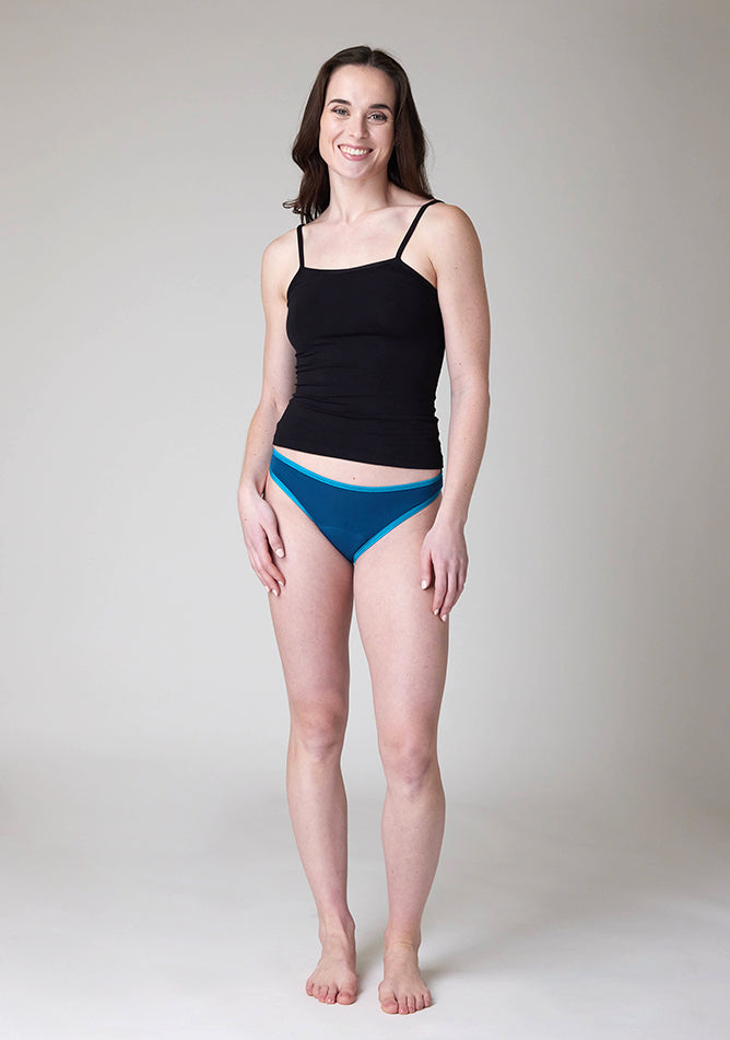 Front image of a five foot nine, size 8 model wearing Ugly Pants' Teal Bikini Brief period pants in light to moderate absorbency, paired with a black cami top. 
