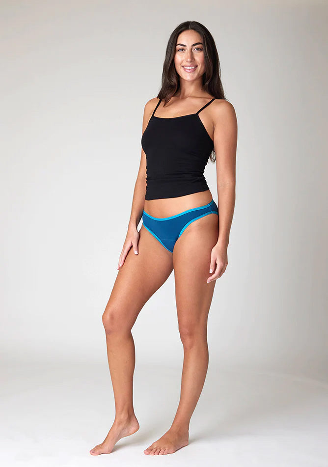 Quarter front image of a five foot ten, size 10 model wearing Ugly Pants' Teal Bikini Brief period Pants in moderate  to heavy absorbency, paired with a black cami top