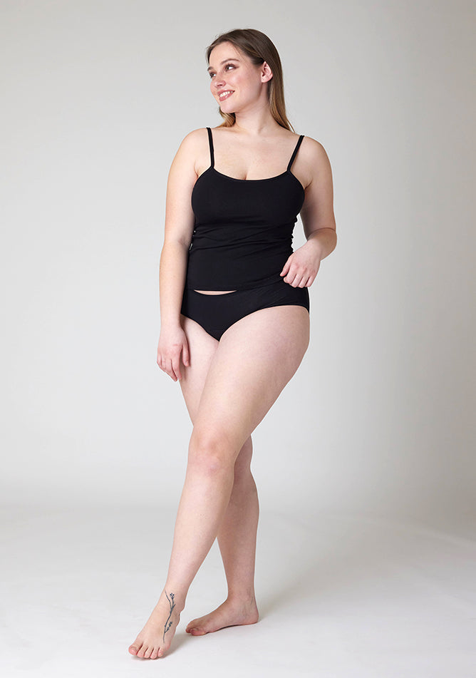 Quarter front image of a five foot five, size 14 model wearing Ugly Pants' Black Hipster Brief Period Pants in light to moderate  absorbency, paired with a black cami top