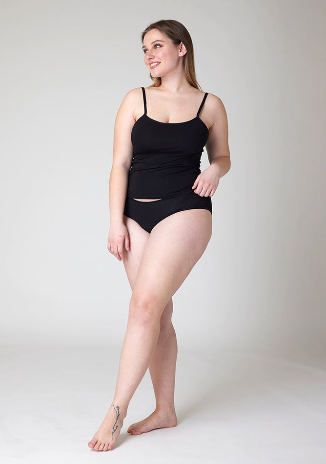 Quarter front image of a five foot five, size 14 model wearing Ugly Pants' Black Hipster Brief Period Pants in moderate to heavy absorbency, paired with a black cami top