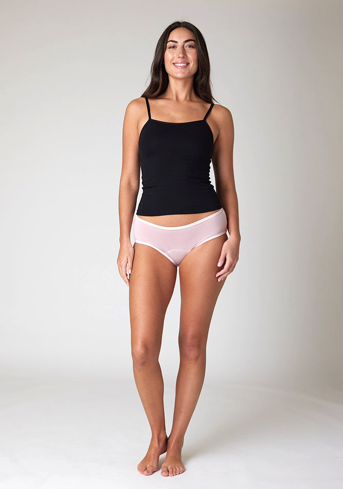 Front image of a five foot ten, size 10 model wearing Ugly Pants' Blush Hipster Brief Period Pants in light to moderate  absorbency, paired with a black cami top