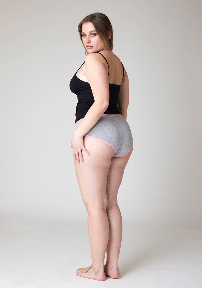 Quarter back image of a five foot five, size 14 model wearing Ugly Pants' Grey Hipster Brief Period Pants with light pink elastic in light to moderate  absorbency, paired with a black cami top