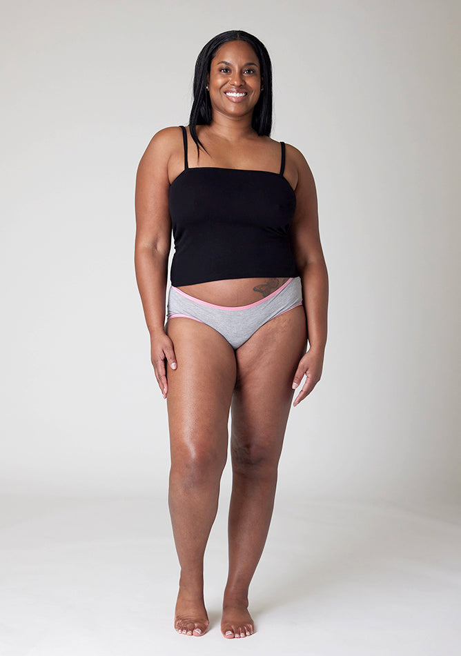 Front image of a five foot five, size 10 model wearing Ugly Pants' Grey Hipster Brief Period Pants with light pink elastic in moderate to heavy absorbency, paired with a black cami top