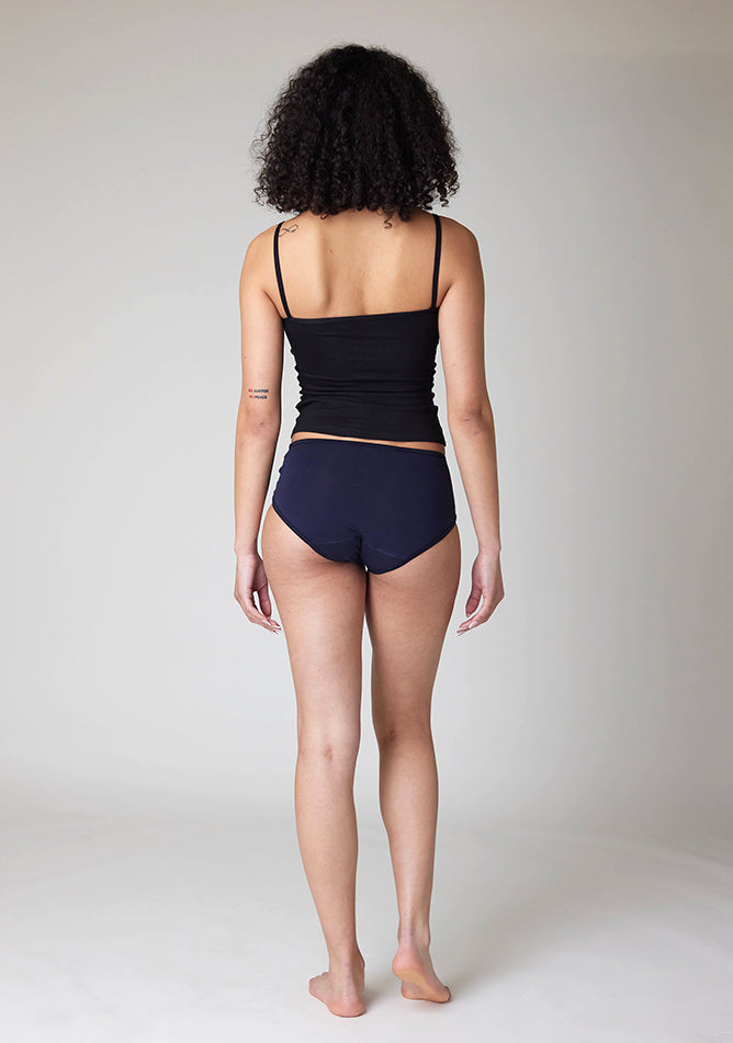Back image of a five foot ten, size 10 model wearing Ugly Pants' Navy Hipster Brief Period Pants in light to moderate  absorbency, paired with a black cami top