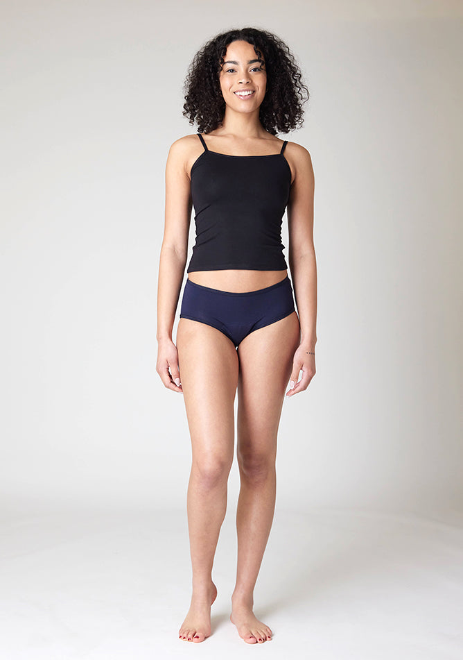 Front image of a five foot ten, size 10 model wearing Ugly Pants' Navy Hipster Brief Period Pants in moderate to heavy absorbency, paired with a black cami top
