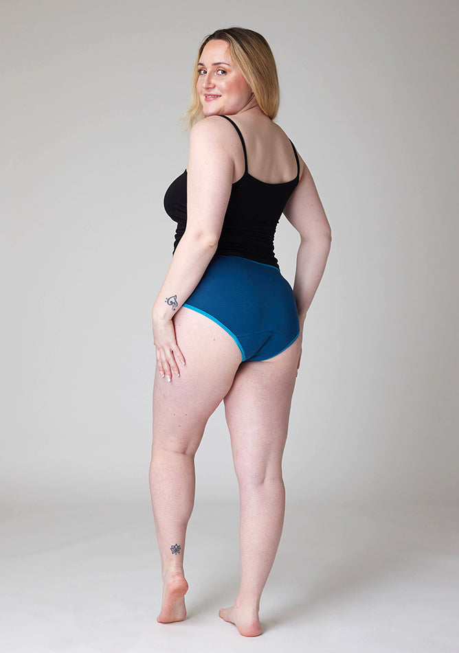 Quarter back image of a five foot three, size 12 model wearing Ugly Pants' Teal Hipster Brief Period Pants in light to moderate  absorbency, paired with a black cami top